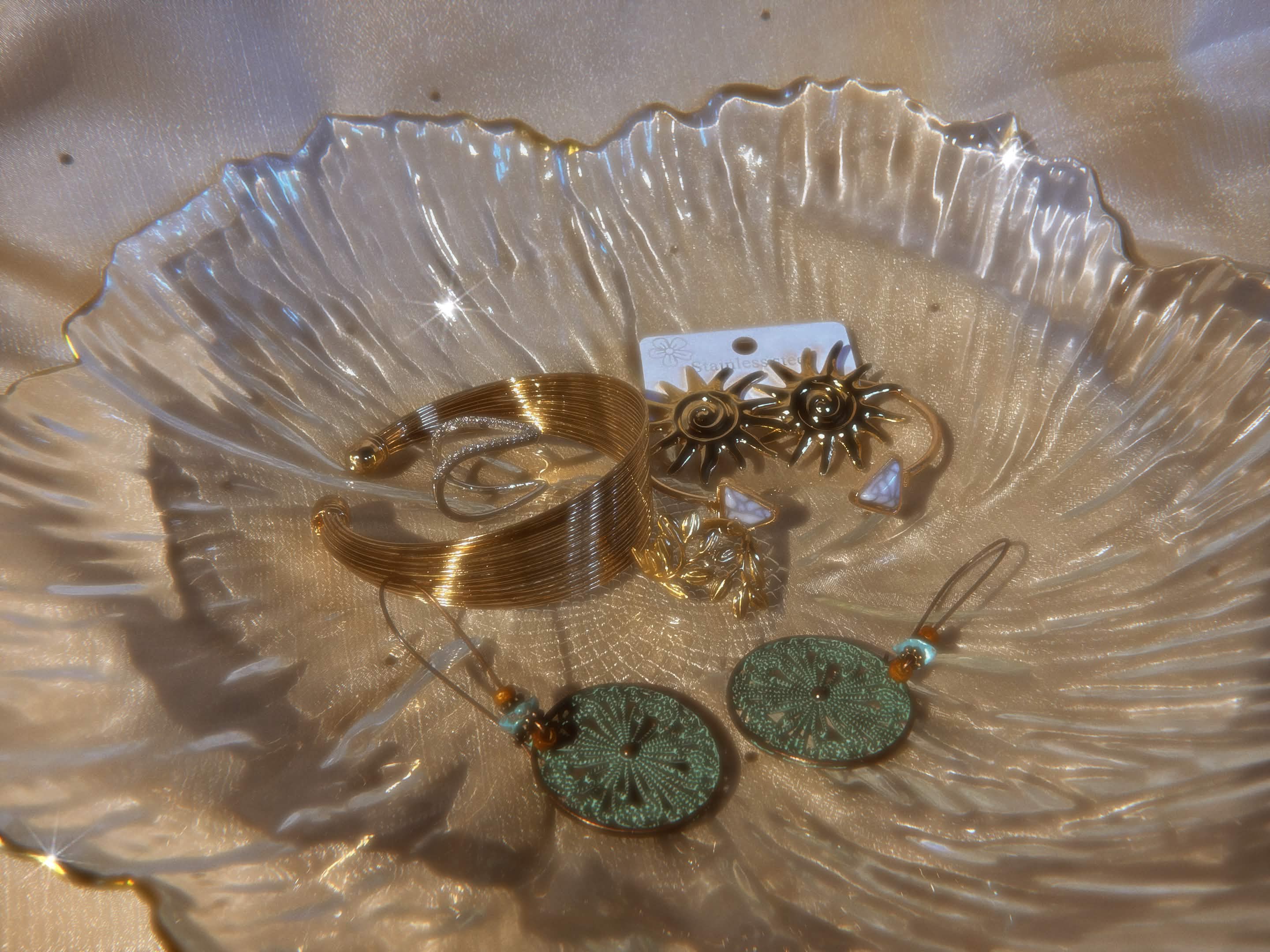 Gold bracelets and sun earrings in crystal bowl