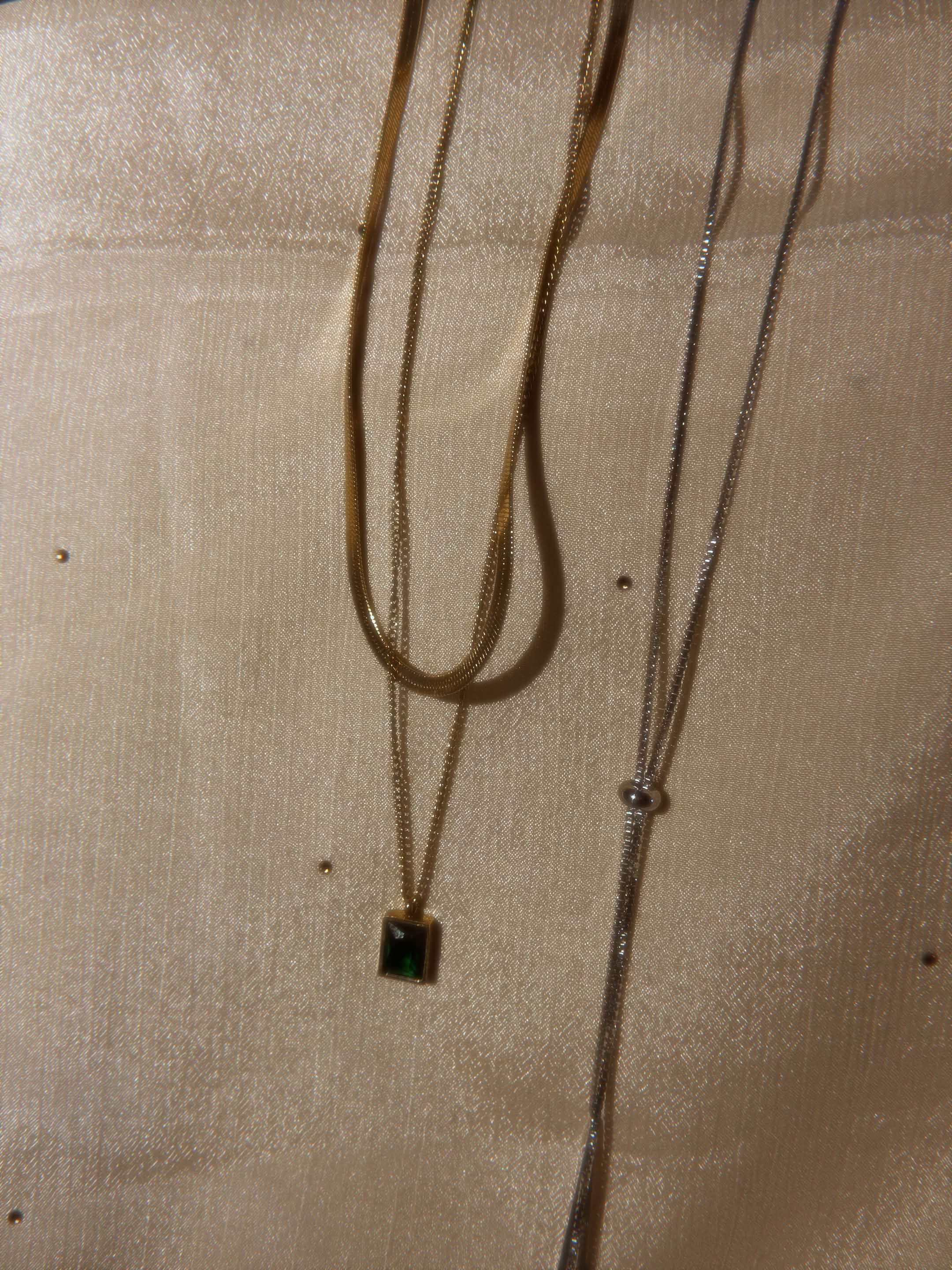 Gold snake chain necklace and silver lariat on golden fabric